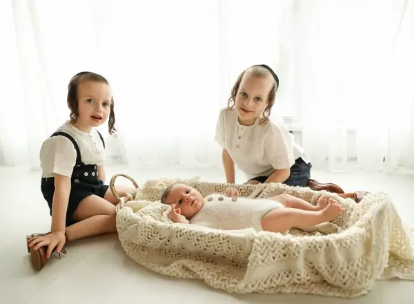 Newborn photography Monsey NY – Two big sisters with their newborn sibling in a woven basket