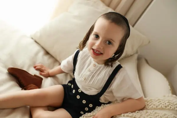 Smiling girl in black overalls lounging on cream pillows, studio photography by Photoholic, Monsey NY